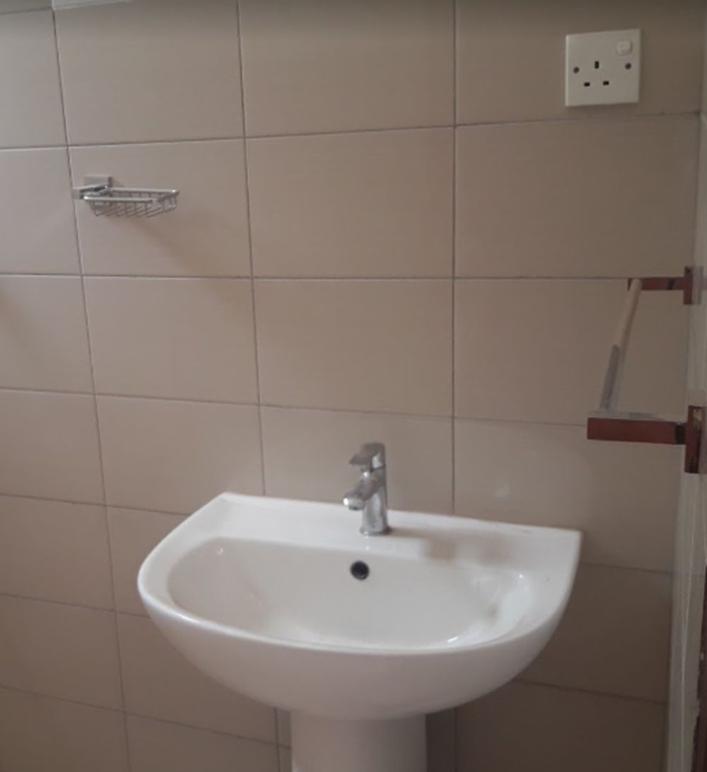 A white pedestal sink with a single faucet in a bathroom with beige tiled walls.