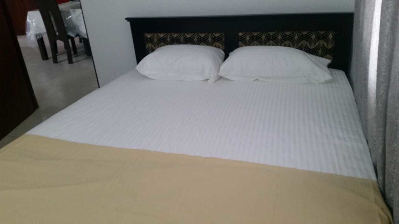 A bed with white linens and a beige blanket.