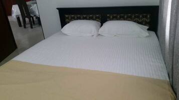 A bed with white linens and a beige blanket.