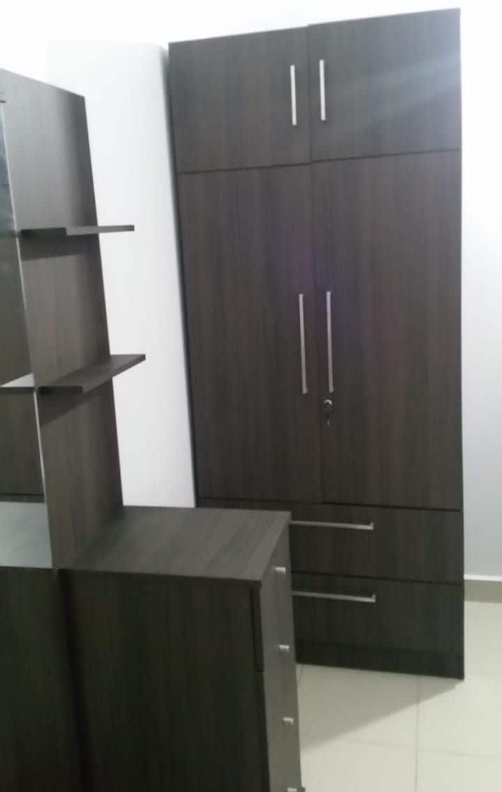 A room with a dark wooden wardrobe, a small table, and a white tiled floor.