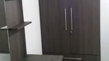 A room with a dark wooden wardrobe, a small table, and a white tiled floor.
