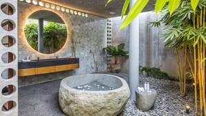 Un baño moderno con una bañera de piedra, un espejo redondo y una planta de bambú.