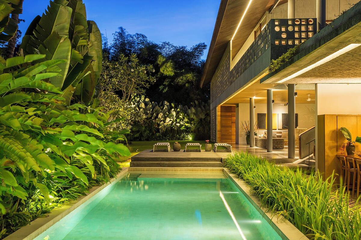 A modern house with a swimming pool, outdoor seating, and lush greenery.