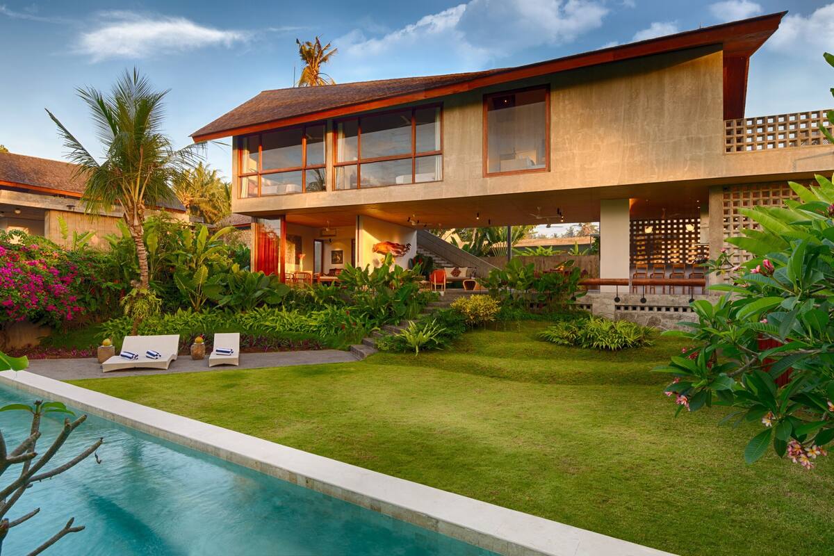 Una casa moderna de dos pisos con piscina, jardín exuberante y zona de estar al aire libre.