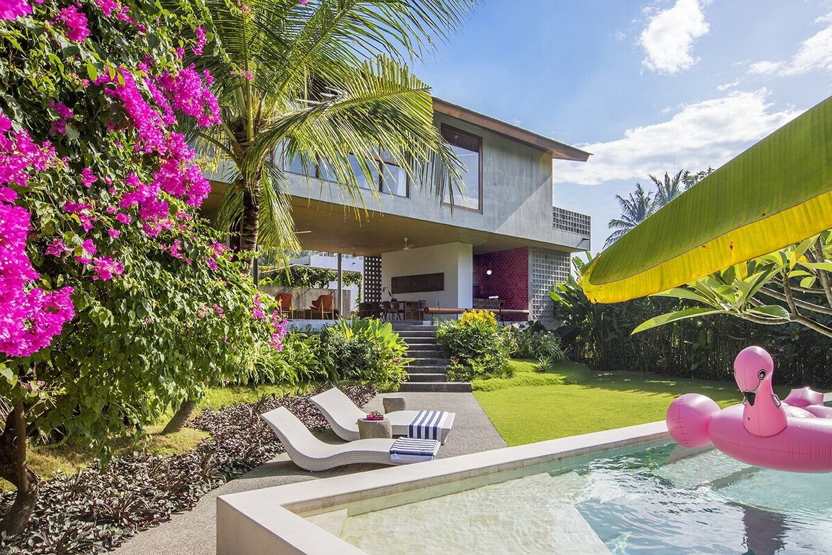 A modern two-story house with a swimming pool, outdoor seating, and lush greenery.