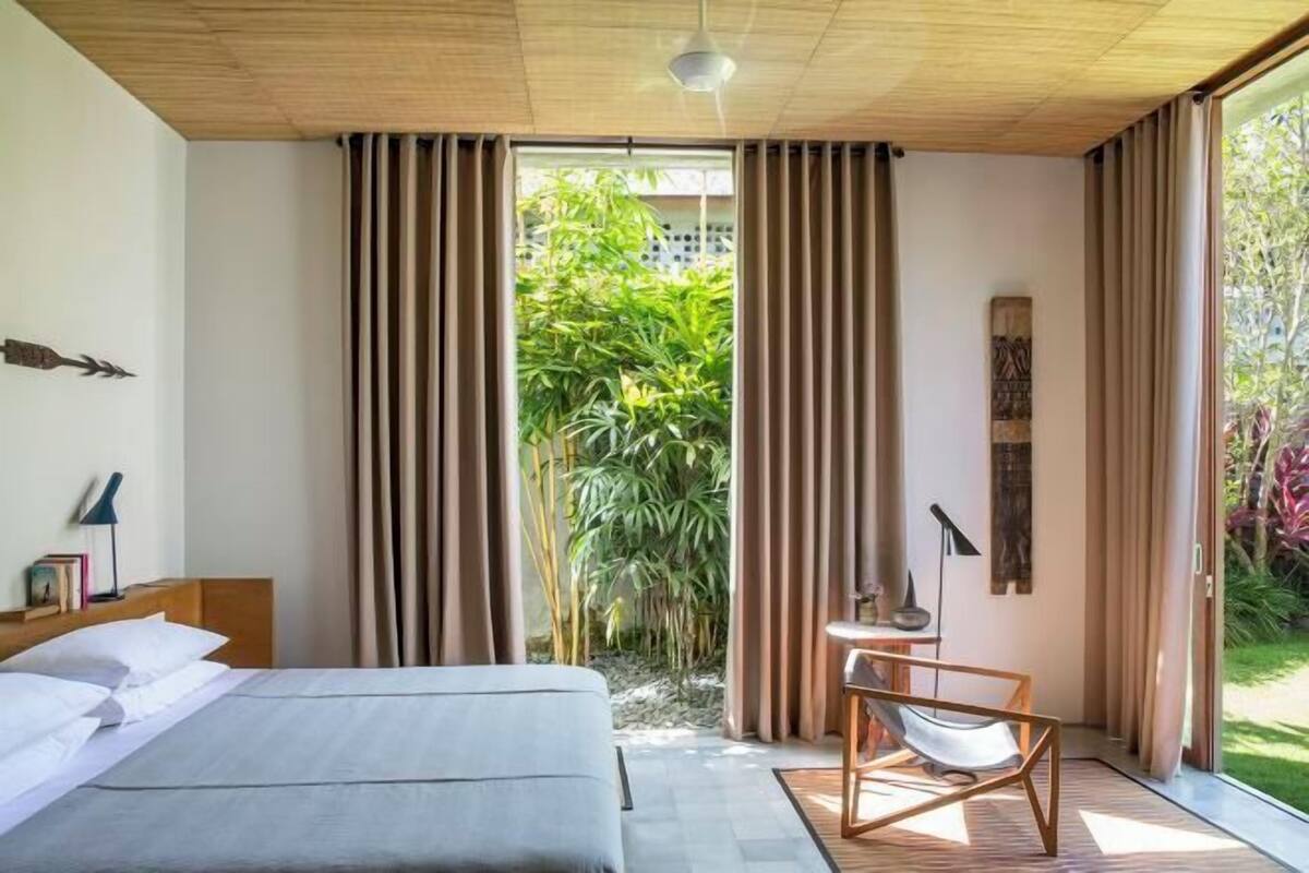 Un dormitorio moderno con una cama grande, una mesita con una silla y vistas a zonas verdes a través de la ventana.