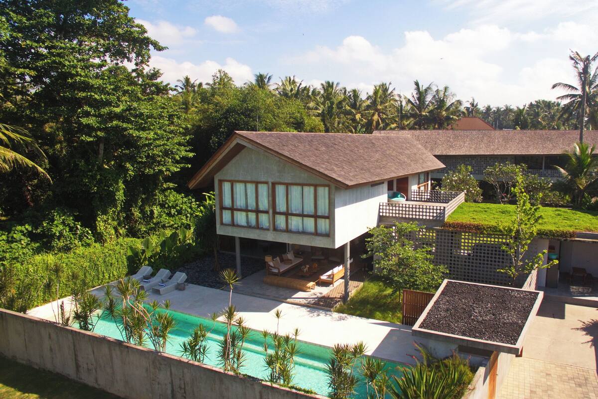 Una villa moderna con piscina, sillas de descanso y un jardín exuberante.