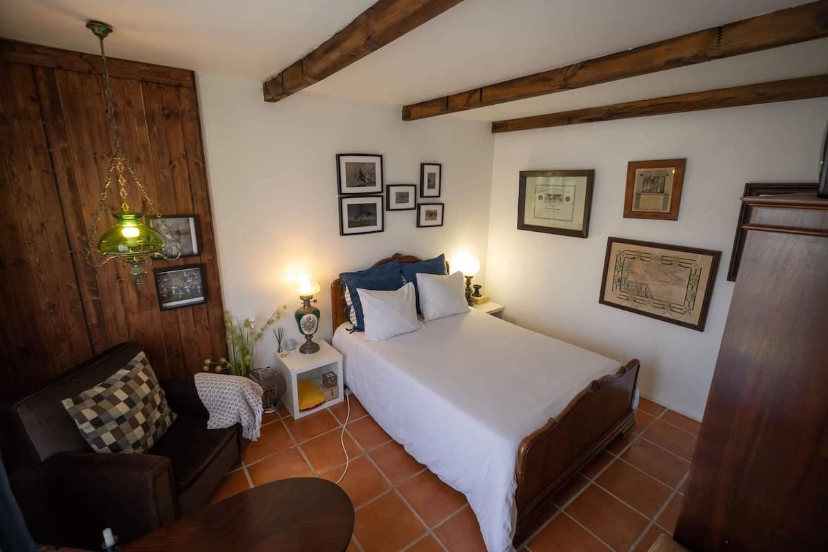 Un dormitorio con techo de madera, una cama con ropa de cama blanca, una mesita de noche de madera con una lámpara y un armario de madera.
