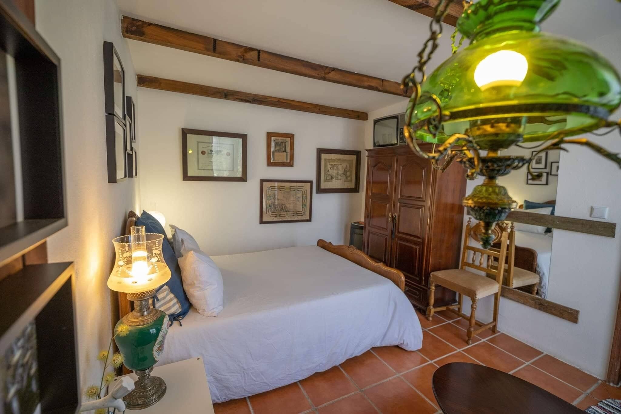 A bedroom with a bed, a wooden chair, a table with a lamp, and a wardrobe.