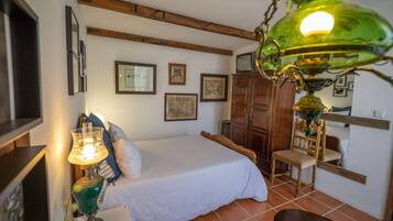 A bedroom with a bed, a wooden chair, a table with a lamp, and a wardrobe.