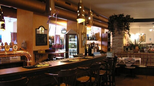 Una zona de bar con una barra larga, varios taburetes y un pilar de ladrillo.