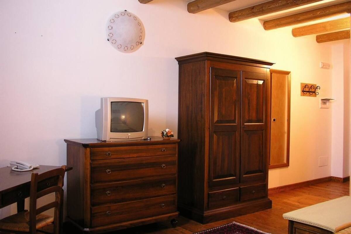 Een kamer met een houten kastje, een televisie erbovenop, een houten stoel en een kamerbreed tapijt met dessin.