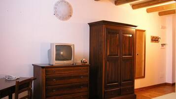 Una stanza con un armadio in legno, una televisione sopra, una sedia in legno e un tappeto decorato.