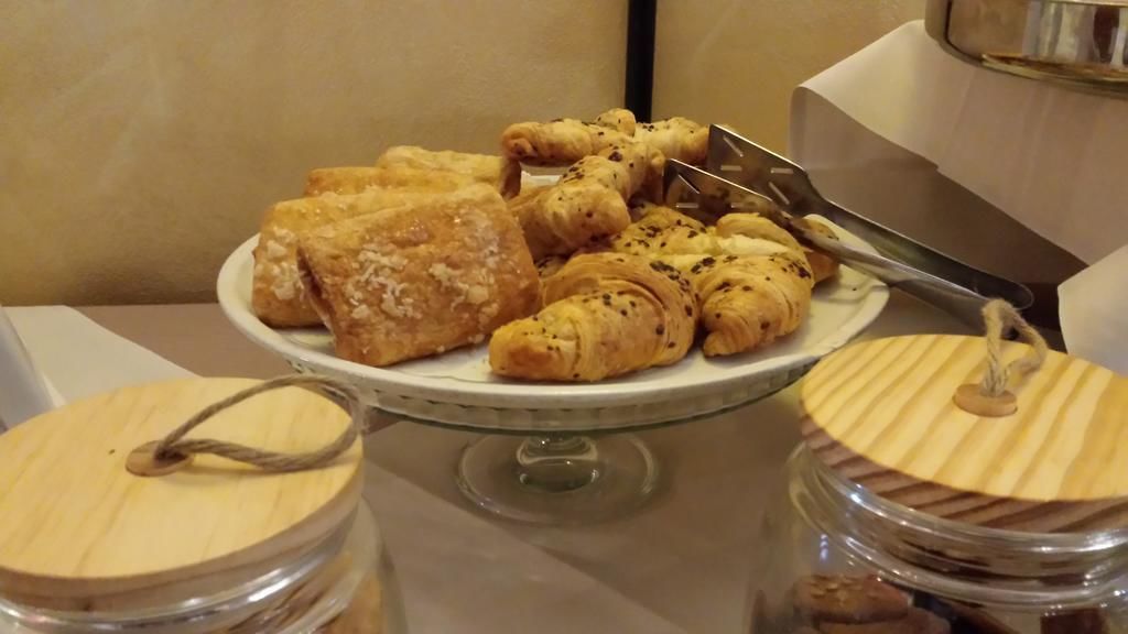 A buffet table with a variety of pastries and bread, including croissants and a large pastry, on a glass stand.