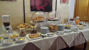 Una mesa de buffet con diversos alimentos y utensilios, incluyendo un dispensador de café, tazones de aperitivos y platos.