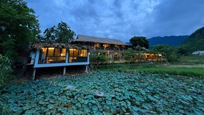 A rustic building with a thatched roof, surrounded by lush greenery and a pond with lily pads. - Mai Chau Sky (Mai Chau)