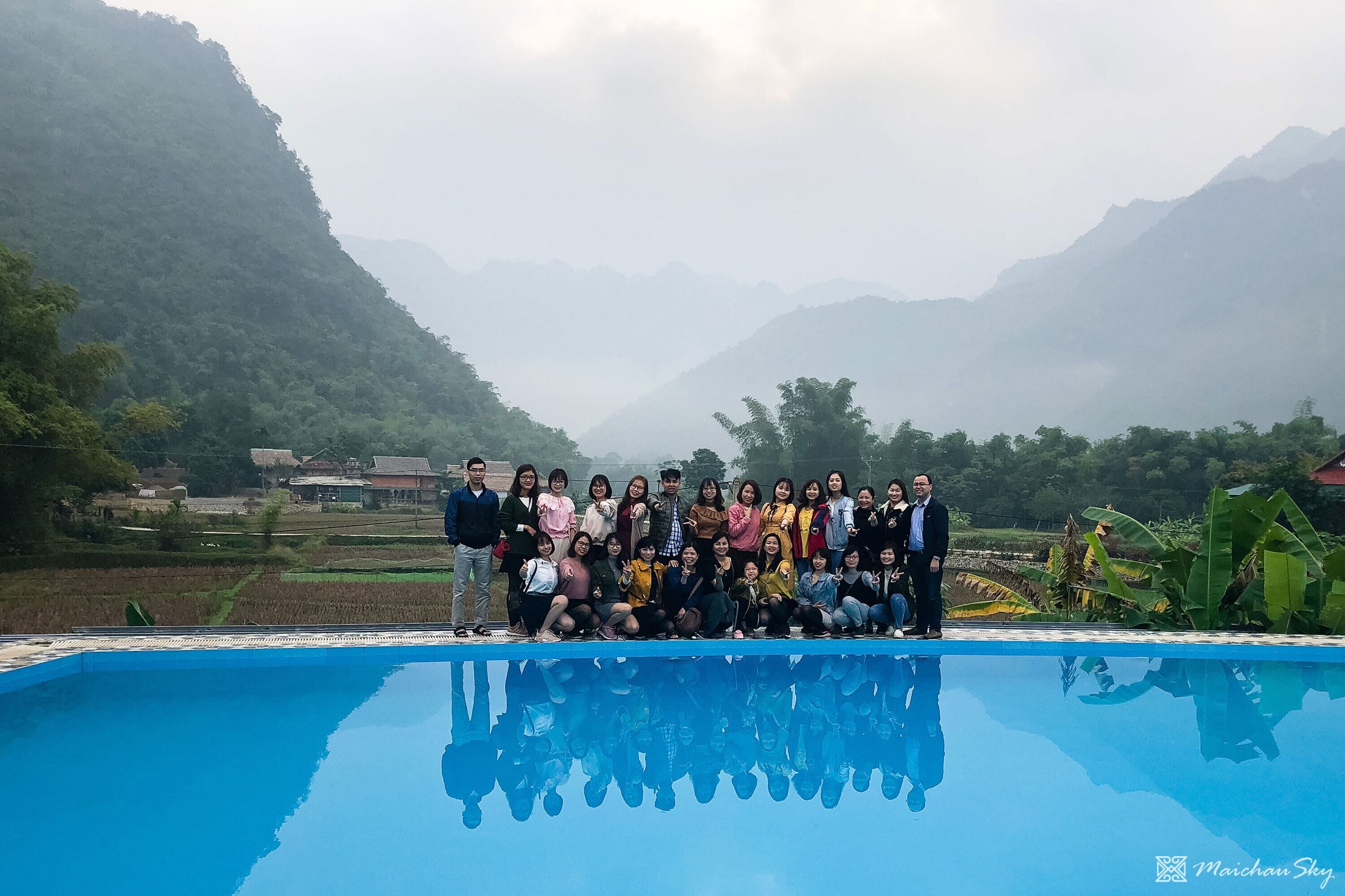 A group of people posing by a swimming pool with a mountainous backdrop.