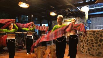 A group of people performing a dance in a room with wooden floors, stone walls, and hanging lights.