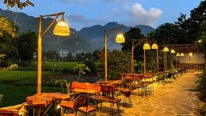 An outdoor dining area with wooden tables and chairs, bamboo lamp posts, and a view of mountains in the background. - Mai Chau Sky (Mai Chau)