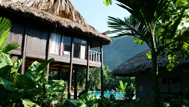 A wooden house with a thatched roof, a balcony, and lush greenery. - Mai Chau Sky (Mai Chau)