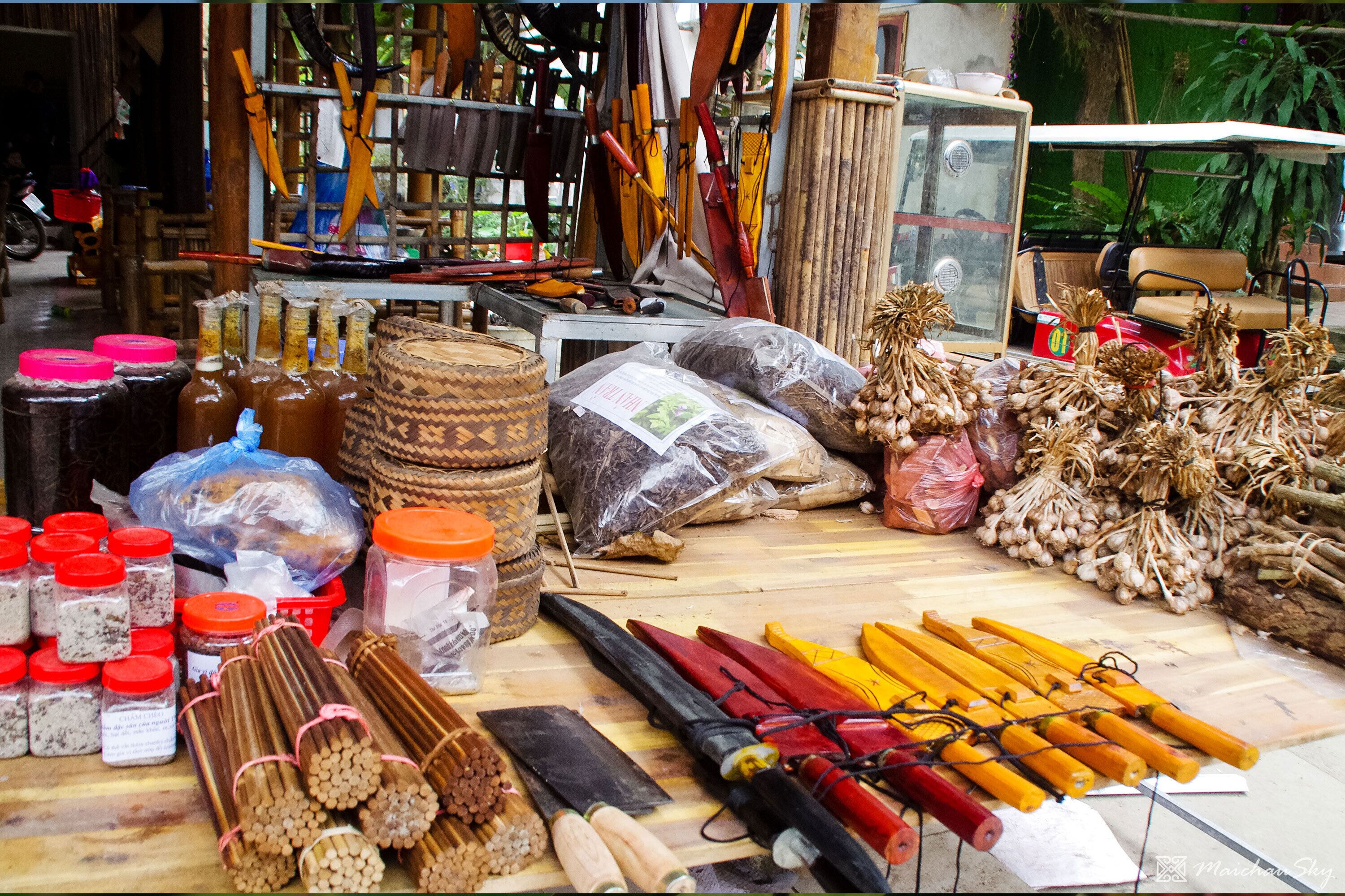 A market stall with various items including bottles, wooden sticks, and bundles of garlic.