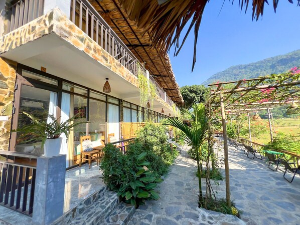 Um hotel com fachada de pedra, grandes janelas, área de estar externa e vista para uma paisagem exuberante.