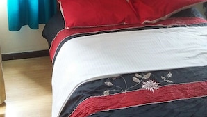 Ein Schlafzimmer mit einem hölzernen Kopfteil, einem Bett mit rot-weißer Bettwäsche und einem blauen Vorhang.