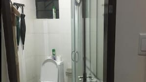 Ein Badezimmer mit Toilette, einer Glasdusche und einem kleinen Fenster über der Toilette.