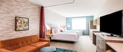 Una habitación de hotel con sofá, cama, escritorio, televisor y ventana.