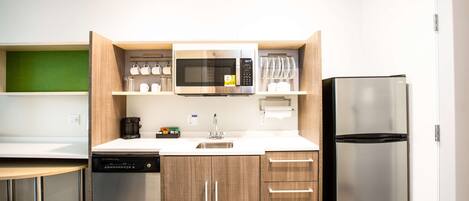 Une cuisine compacte équipée d’un lave-vaisselle, d’un four à micro-ondes, d’un réfrigérateur et de meubles de rangement en bois.
