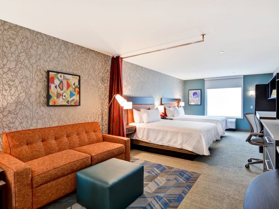 A hotel room with a sofa, two beds, a desk, and a TV.