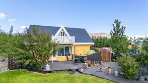 Et moderne hus med stor terrasse, en indhegnet have og et bjerg i baggrunden.
