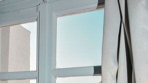 A window with a view of a coastal landscape, including a mountain and buildings. - Anamar Patmos (Patmos)