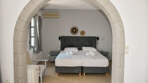 A bedroom with a bed, a nightstand, a small table, and a window with curtains. - Anamar Patmos (Patmos)