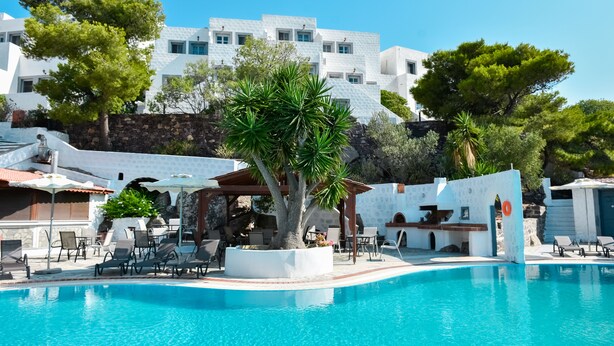 A pool area with lounge chairs, a pergola, and a white building in the background. - Anamar Patmos (Patmos)