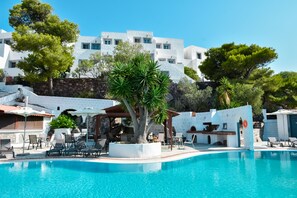 A pool area with lounge chairs, a pergola, and a white building in the background. - Anamar Patmos (Patmos)