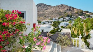 A coastal town with white buildings, a rocky hill in the background, and pink flowers in the foreground. - Anamar Patmos (Patmos)