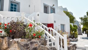 A white building with a staircase, red door, and stone wall with red flowers. - Anamar Patmos (Patmos)
