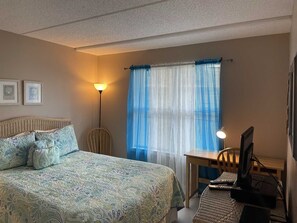 A bedroom with a bed, a desk, and a chair. There are two framed pictures on the wall.