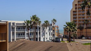 Un hotel de varios pisos con balcones, palmeras y vista despejada a la playa.