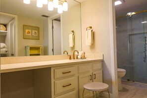 Een badkamer met een grote spiegel, een wastafel met gouden details, een toilet en een douchecabine van glas.