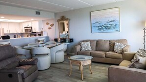 Een moderne woonkamer met een bank, fauteuils, een klein tafeltje en een keuken in de achtergrond.