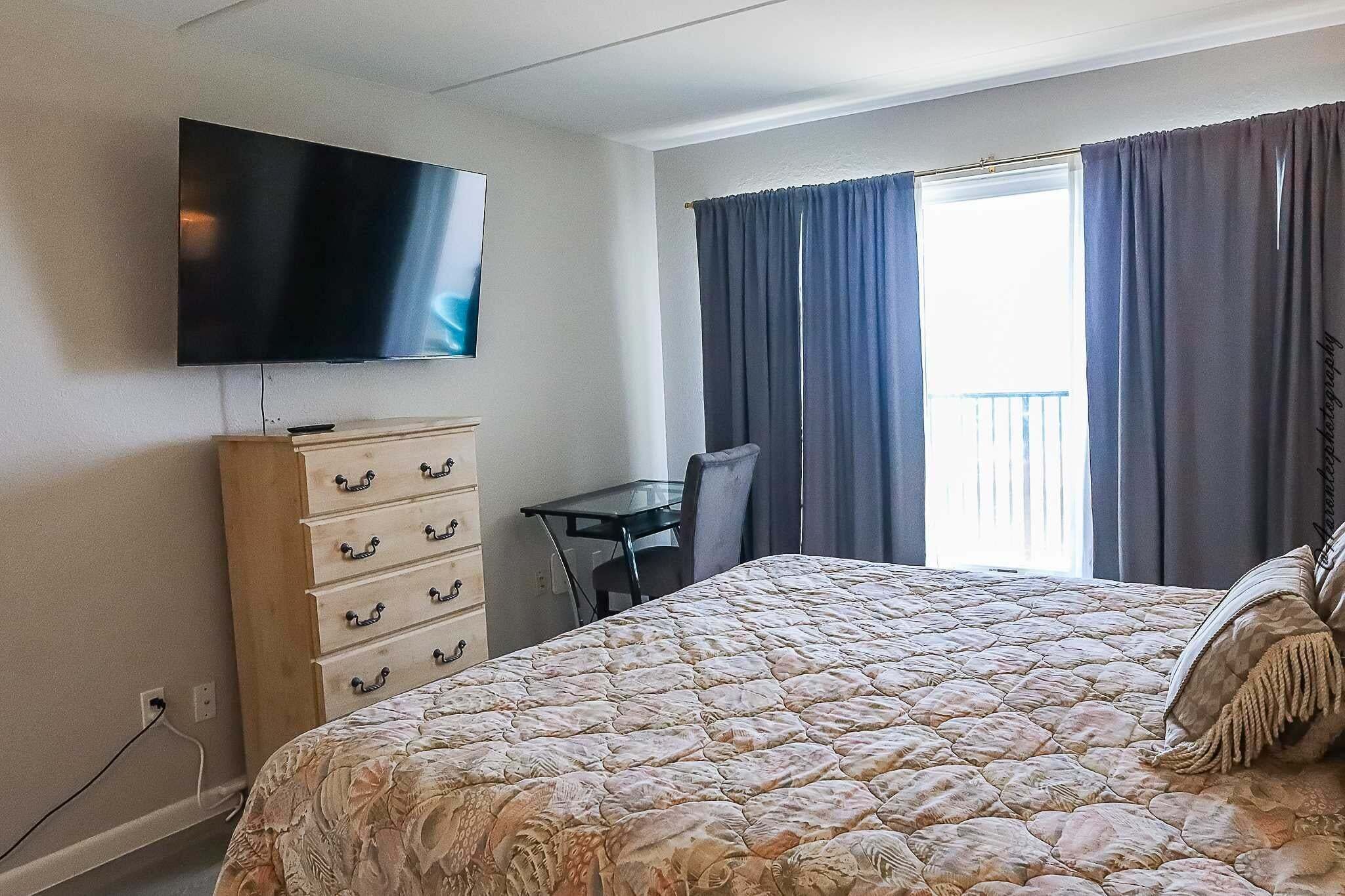 A hotel room with a bed, a TV mounted on the wall, a desk, and a chair.