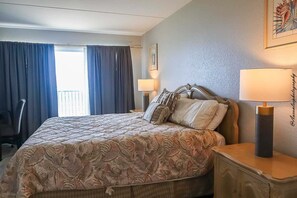 Hotelkamer met een bed, twee bedlampen, een stoel, een raam met gordijnen en een ingelijst schilderij aan de muur.