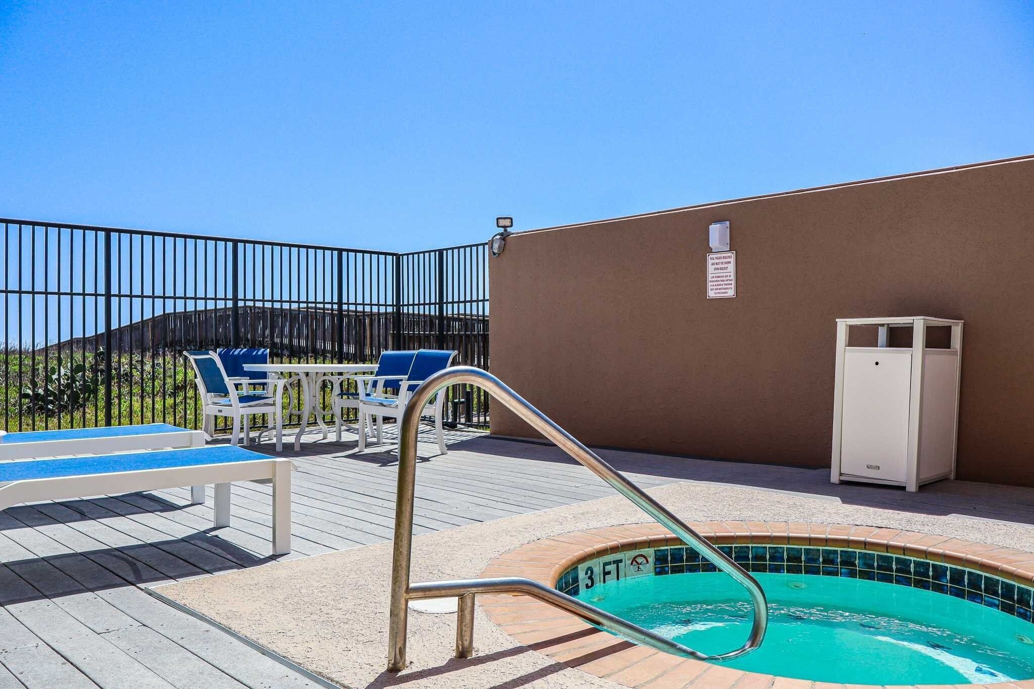 A rooftop pool area with a 3 FT depth marker, lounge chairs, a table, and a white cabinet.