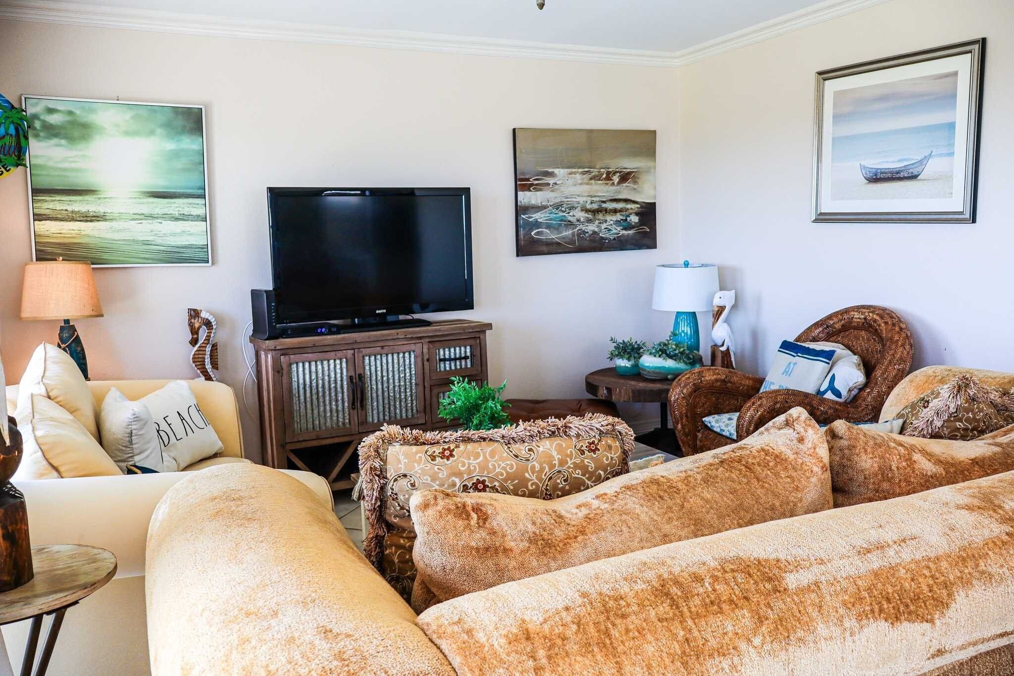 A living room with a flat-screen TV, beige sofas, a wooden cabinet, and wall art.
