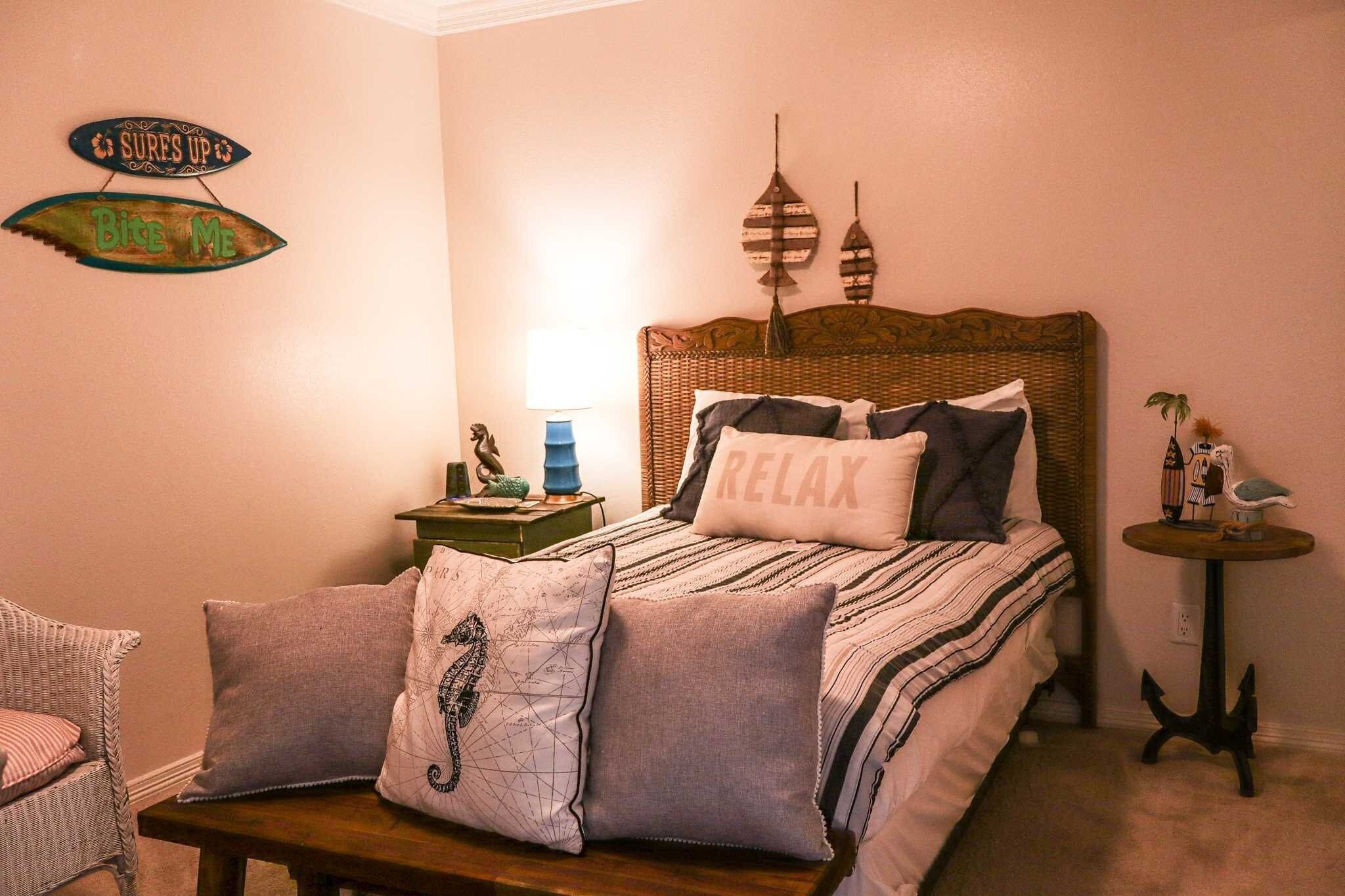 A bedroom with a bed, pillows, a nightstand, a lamp, and wall decorations.