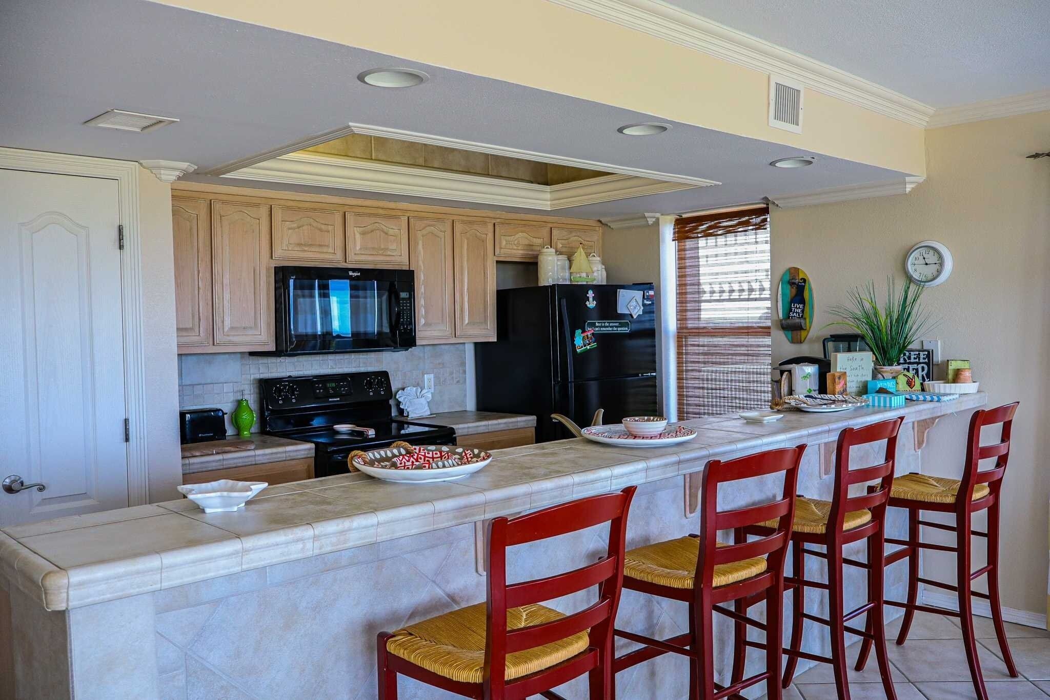 A modern kitchen with a marble countertop, wooden cabinets, a black refrigerator, and a built-in microwave.