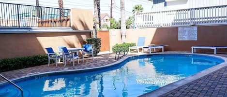 A swimming pool with lounge chairs, a fenced area, and a sign listing amenities.