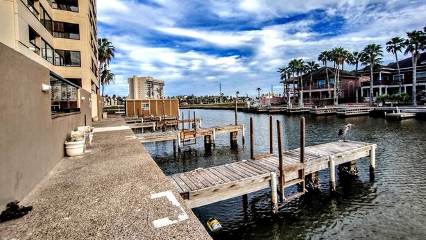 A waterfront property with a dock, a building with multiple floors, and a clear sky.